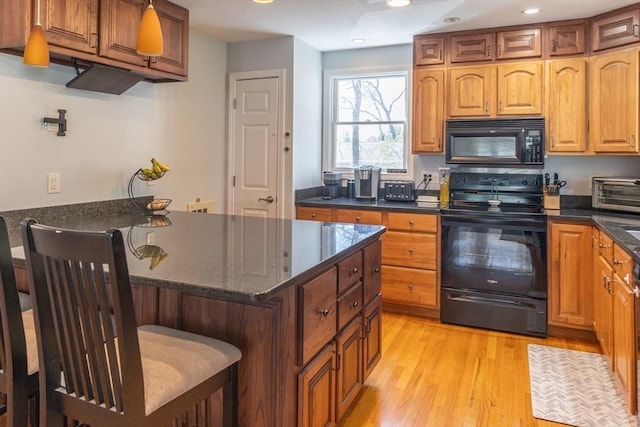 kitchen featuring a breakfast bar area, light wood-style flooring, dark stone counters, a toaster, and black appliances