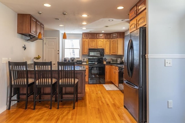 kitchen with a breakfast bar area, dark countertops, black appliances, a peninsula, and light wood-style floors