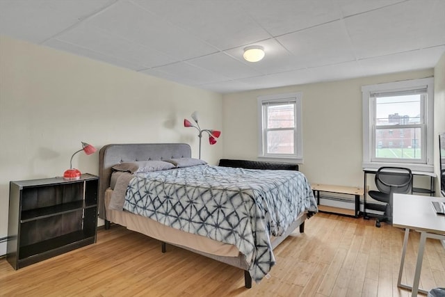 bedroom featuring light wood-type flooring, a baseboard radiator, and multiple windows