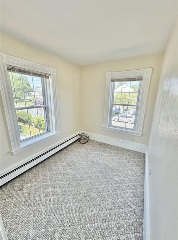 carpeted empty room featuring a baseboard heating unit and baseboards