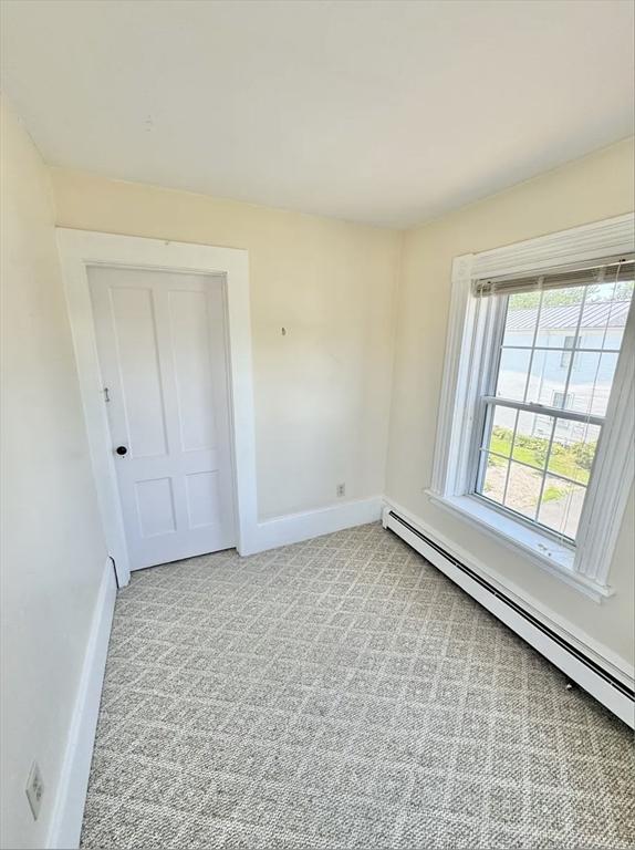 spare room with a baseboard heating unit, light colored carpet, and baseboards