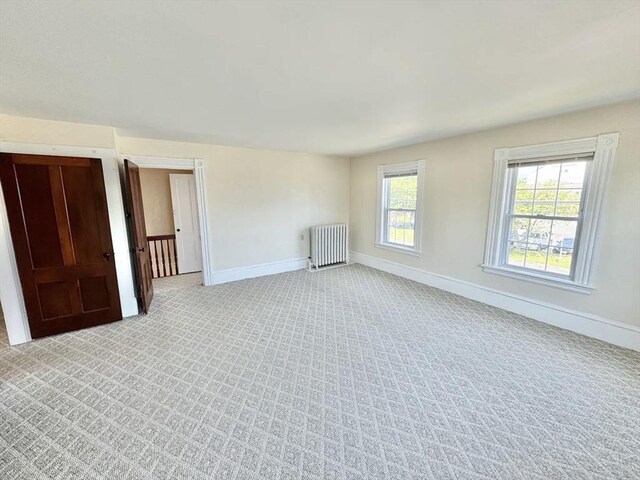 empty room with baseboards, light colored carpet, and radiator