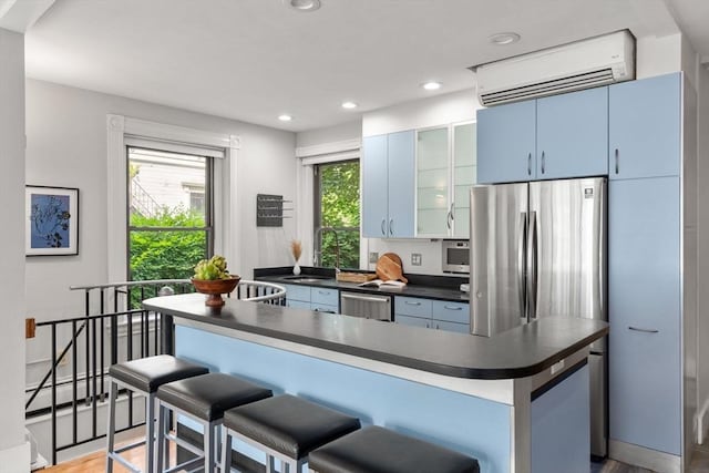 48 Kent St Unit 1, Brookline, MA 02445 - kitchen featuring dark countertops, an AC wall unit, stainless steel appliances, a sink, and a kitchen breakfast bar