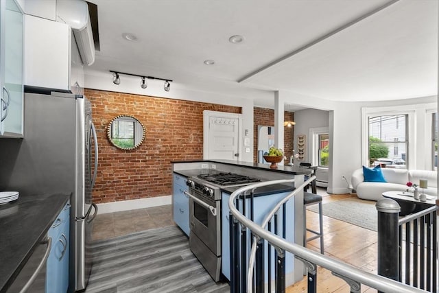 48 Kent St Unit 1, Brookline, MA 02445 - kitchen with brick wall, stainless steel appliances, dark countertops, baseboards, and wood finished floors