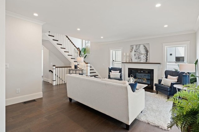 living room featuring crown molding, dark wood-style flooring, a glass covered fireplace, baseboards, and visible vents