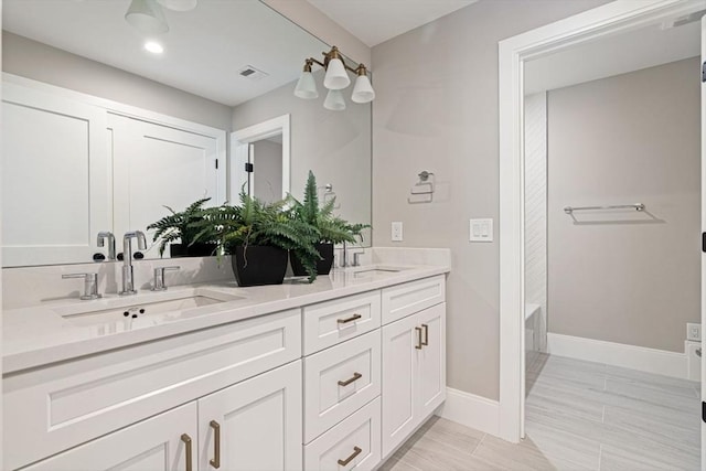 bathroom with a sink, baseboards, double vanity, and visible vents