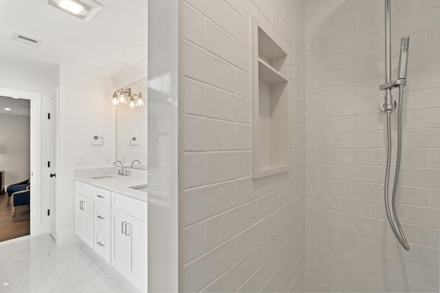 bathroom featuring connected bathroom, a tile shower, a sink, double vanity, and visible vents
