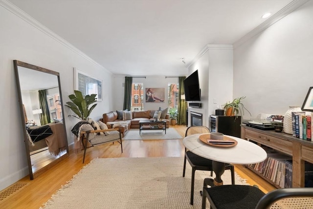 living room with light wood-style flooring, baseboards, crown molding, and a glass covered fireplace