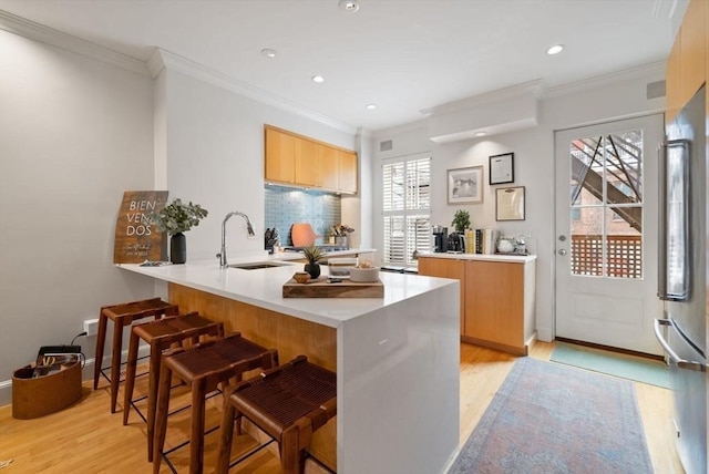 kitchen with a breakfast bar, a peninsula, light countertops, light wood-style floors, and a sink