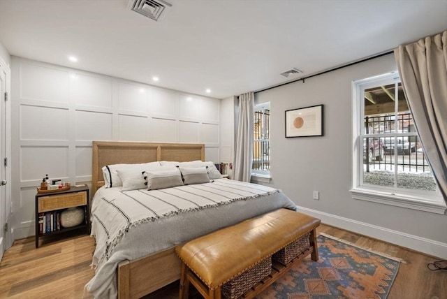 bedroom with light wood-type flooring, visible vents, a decorative wall, and baseboards