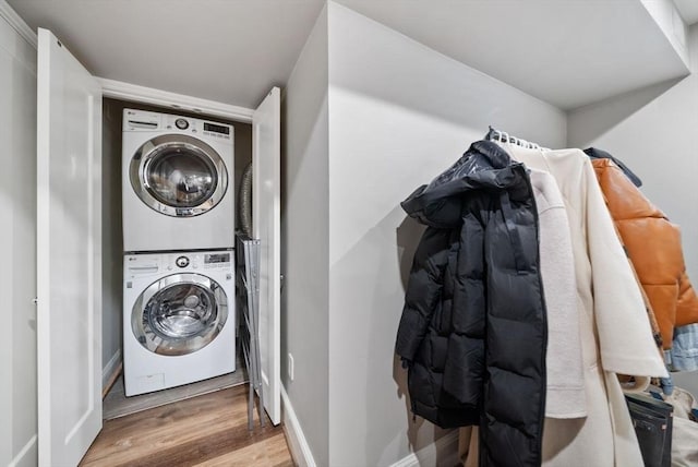 laundry area featuring stacked washer and dryer, laundry area, baseboards, and wood finished floors