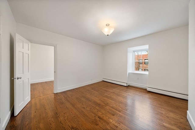 spare room featuring baseboard heating, a baseboard radiator, wood finished floors, and baseboards