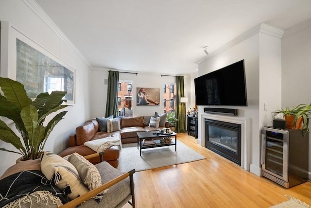 living room with wine cooler, a glass covered fireplace, crown molding, and wood finished floors