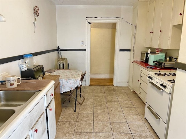 kitchen with light countertops, light tile patterned flooring, white cabinets, a sink, and white gas range oven