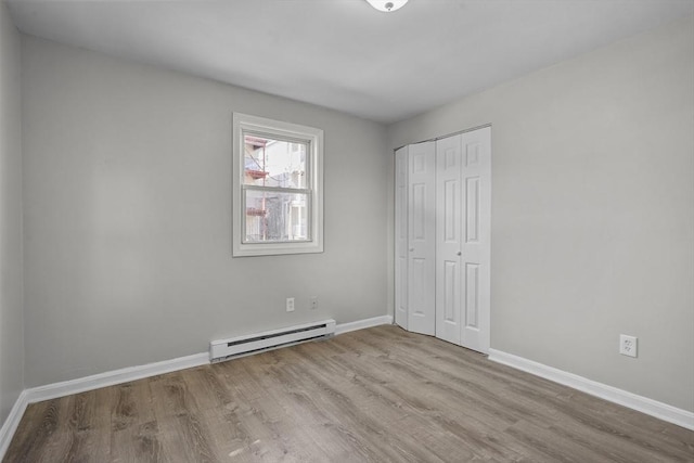 unfurnished bedroom featuring a closet, light wood-type flooring, and a baseboard heating unit