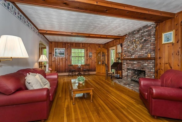 living area featuring wooden walls, hardwood / wood-style floors, beam ceiling, and a brick fireplace