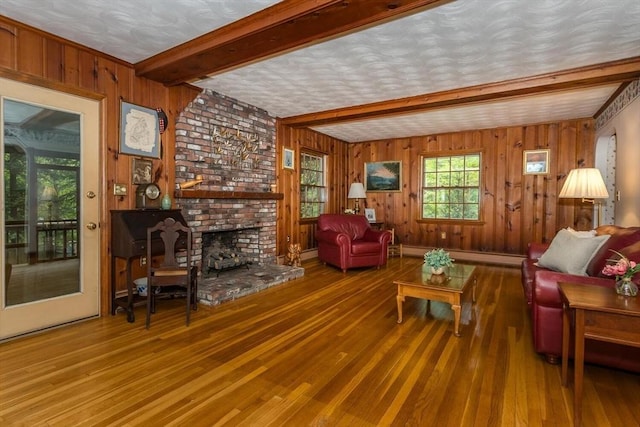 living room featuring beam ceiling, wood-type flooring, baseboard heating, wooden walls, and a fireplace