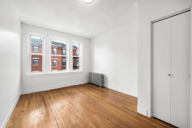 unfurnished bedroom featuring a closet, radiator heating unit, and hardwood / wood-style flooring