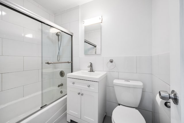 full bathroom featuring vanity, toilet, tile walls, and shower / bath combination with glass door