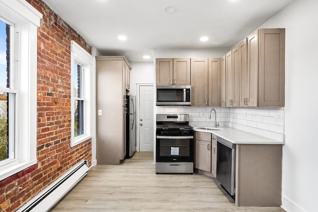 kitchen with sink, stainless steel appliances, brick wall, a baseboard heating unit, and light wood-type flooring