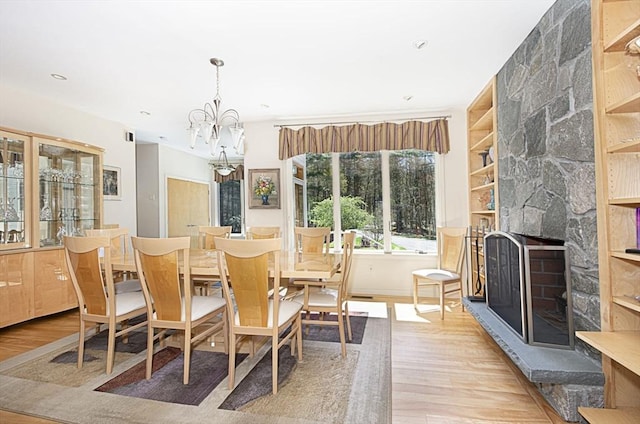 dining area with wood finished floors, a chandelier, a stone fireplace, built in features, and recessed lighting