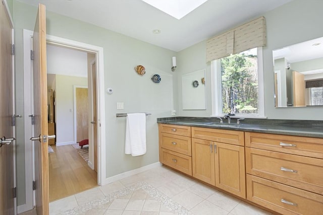 bathroom featuring tile patterned flooring, vanity, a skylight, and baseboards