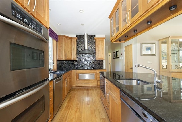 kitchen featuring a sink, stainless steel appliances, a warming drawer, light wood-style flooring, and wall chimney exhaust hood