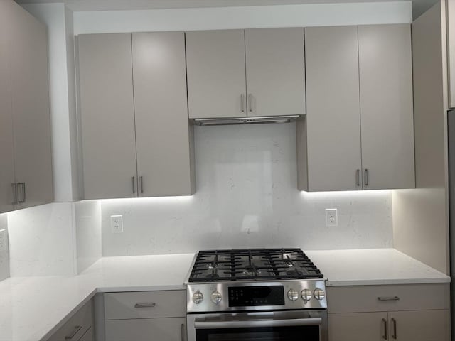 kitchen featuring tasteful backsplash, gray cabinets, stainless steel gas range oven, and ventilation hood