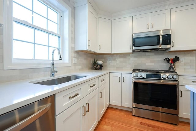 kitchen featuring sink, white cabinetry, light wood-type flooring, stainless steel appliances, and backsplash