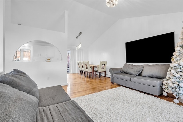 living room featuring an inviting chandelier, wood-type flooring, vaulted ceiling, and a baseboard heating unit