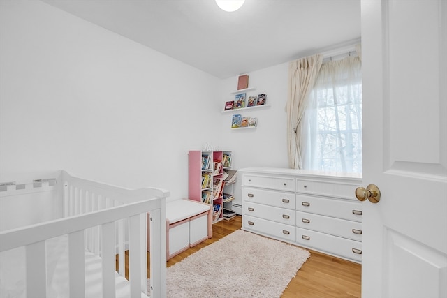 bedroom with light hardwood / wood-style flooring, a nursery area, and a baseboard heating unit