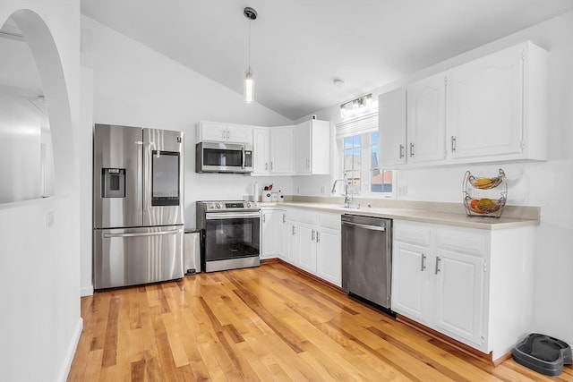 kitchen with pendant lighting, stainless steel appliances, vaulted ceiling, and white cabinetry