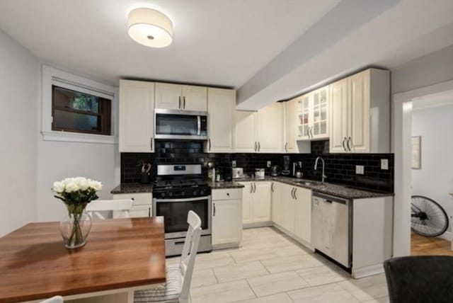 15 Trowbridge St Unit 12A, Cambridge, MA 02139 - kitchen with appliances with stainless steel finishes, decorative backsplash, dark countertops, a sink, and glass insert cabinets