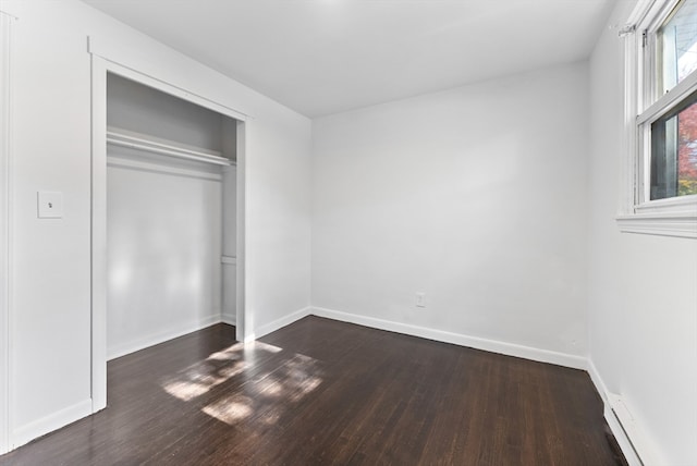 unfurnished bedroom featuring dark wood-type flooring, a closet, and a baseboard heating unit