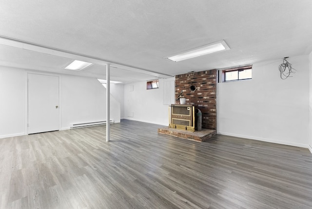 basement featuring hardwood / wood-style floors, a baseboard heating unit, a textured ceiling, and a wood stove