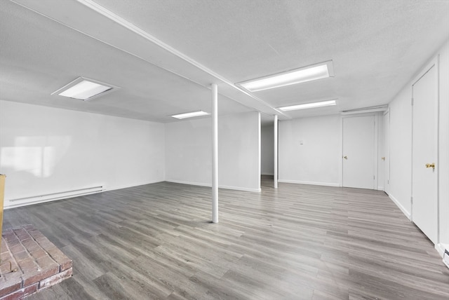 basement with hardwood / wood-style floors, a baseboard heating unit, and a textured ceiling