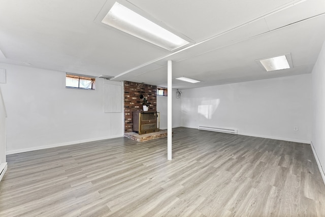 basement featuring baseboard heating, light wood-type flooring, and a wood stove