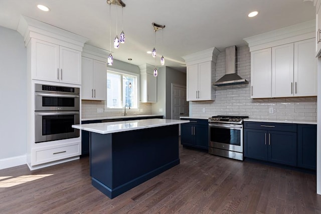 kitchen featuring a center island, light countertops, appliances with stainless steel finishes, wall chimney exhaust hood, and dark wood-style flooring