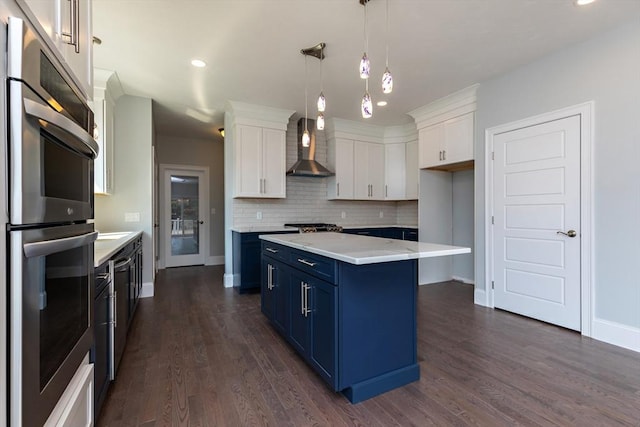 kitchen with wall chimney range hood, double oven, light countertops, white cabinets, and blue cabinets