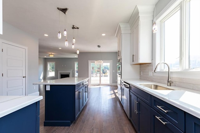 kitchen featuring backsplash, light countertops, hanging light fixtures, blue cabinets, and a sink