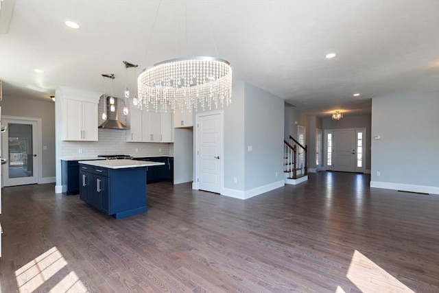 kitchen with a kitchen island, wall chimney range hood, white cabinets, blue cabinets, and dark wood-style flooring