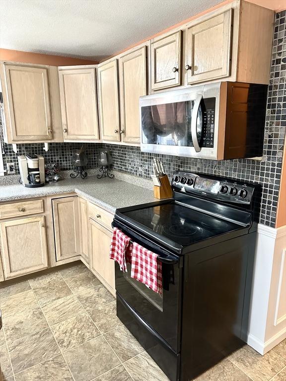 kitchen with backsplash, black electric range, a textured ceiling, and light brown cabinets