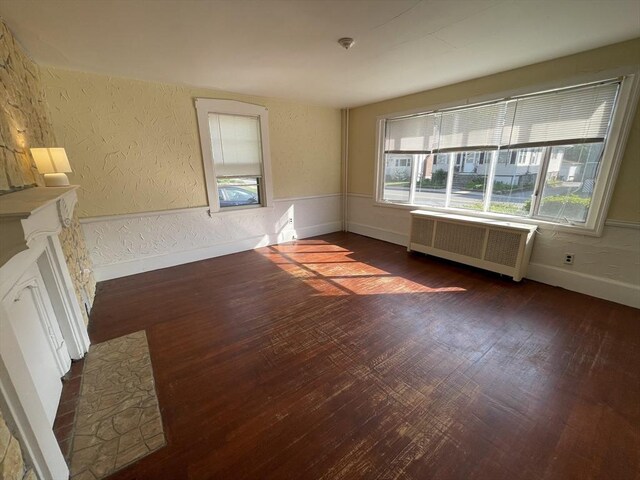 empty room with radiator, plenty of natural light, a textured wall, dark wood finished floors, and baseboards