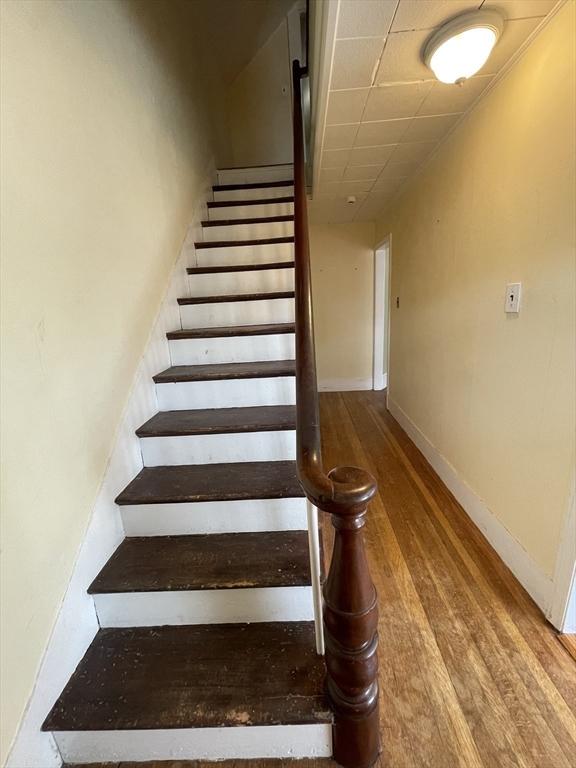 stairs featuring a drop ceiling, wood finished floors, and baseboards