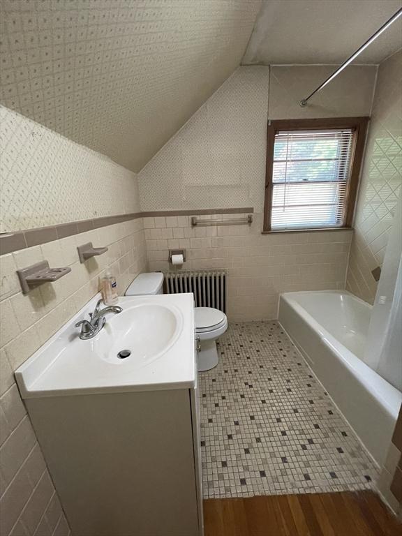full bathroom with radiator heating unit, toilet, tile walls, vanity, and wood finished floors