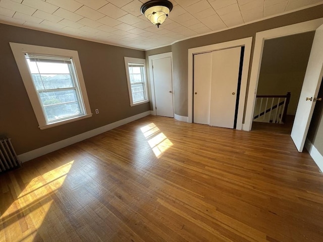 unfurnished bedroom with multiple windows, radiator, wood finished floors, and baseboards