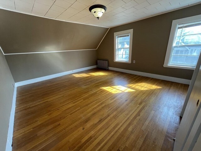 bonus room with radiator, hardwood / wood-style flooring, vaulted ceiling, and baseboards