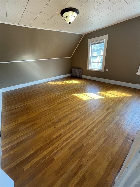 additional living space featuring radiator heating unit, wood-type flooring, baseboards, and lofted ceiling