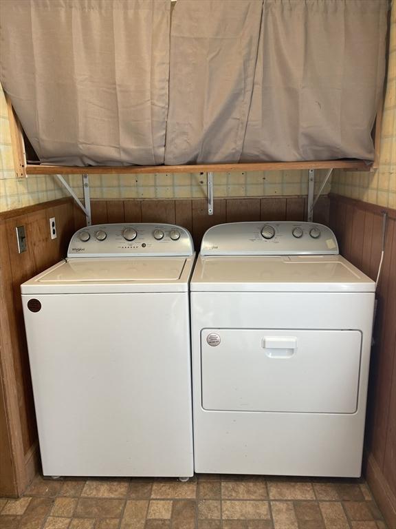 washroom featuring wooden walls, washing machine and clothes dryer, and stone finish flooring
