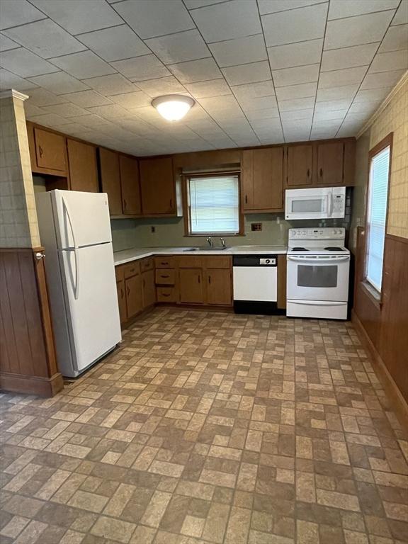 kitchen with white appliances, brick patterned flooring, light countertops, wooden walls, and a sink